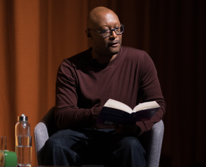 Courttia Newland, seated on stage, reading from his novel, A River Called Time